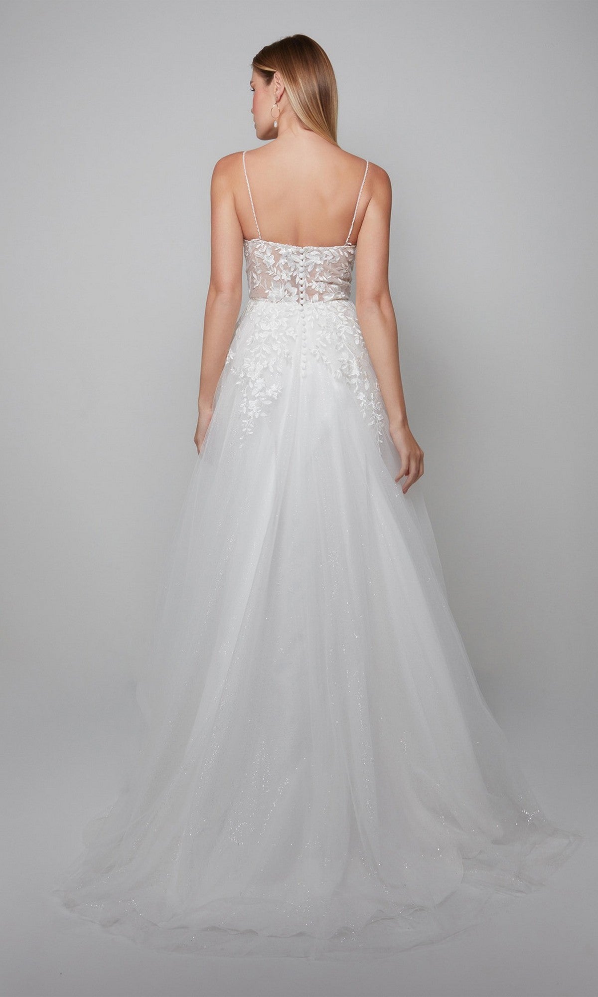 A woman faces away, wearing the Alyce 7079 long white dress, a floor-length gown with thin straps and a sheer lace bodice that epitomizes bridal elegance.